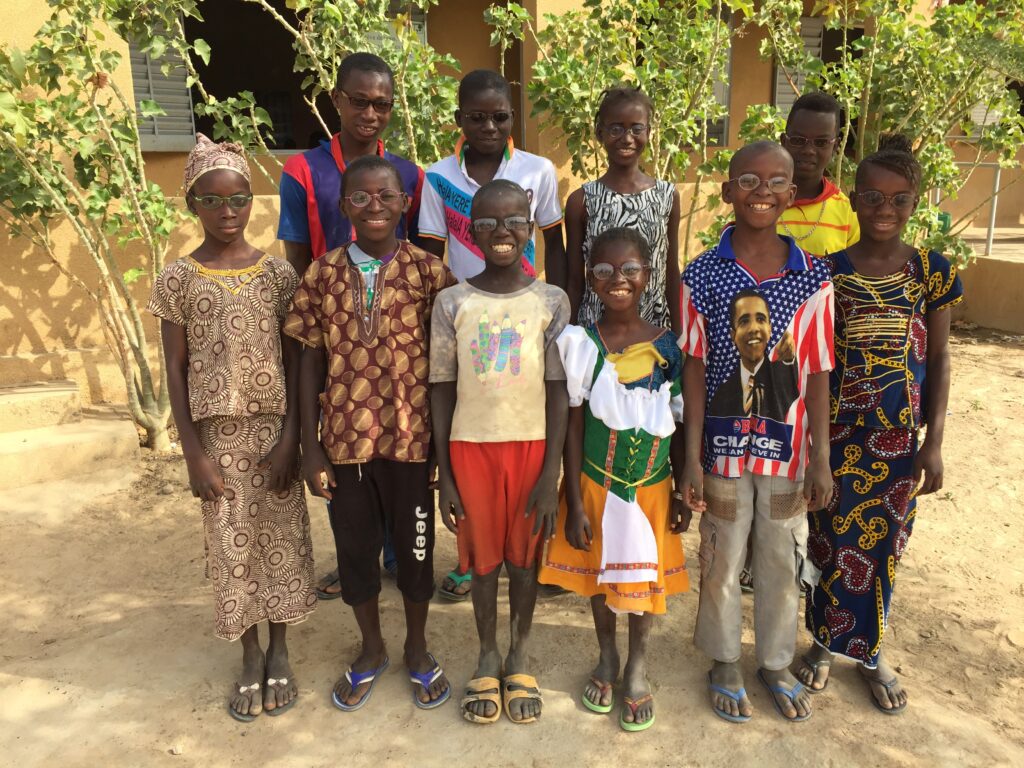 Ten school age children wearing glasses posing outside of school